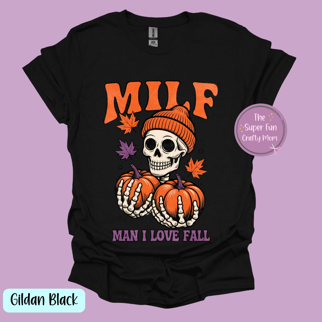 This image features a playful and humorous t-shirt design, titled "Man I Love Fall (MILF)." The shirt showcases a striking graphic of a skeleton dressed in a cap and holding two orange pumpkins, cleverly incorporating the acronym "MILF" into the design.